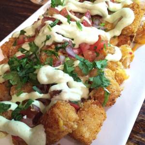 Photo of potato tots with ranch, onion, tomato and lettuce on top.