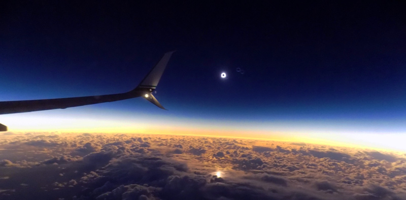 This is a photo of an Alaska Airlines winglet, taken while flying above the clouds. A total solar eclipse is happening in the distance.