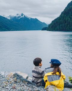 Photo of two children sitting on the shore with a view of mountains in the background.