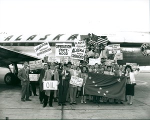 A group of Alaskans standing outside an Alaska Airlines DC-4 jet holding signs advocating for statehood and an Alaska state flag.