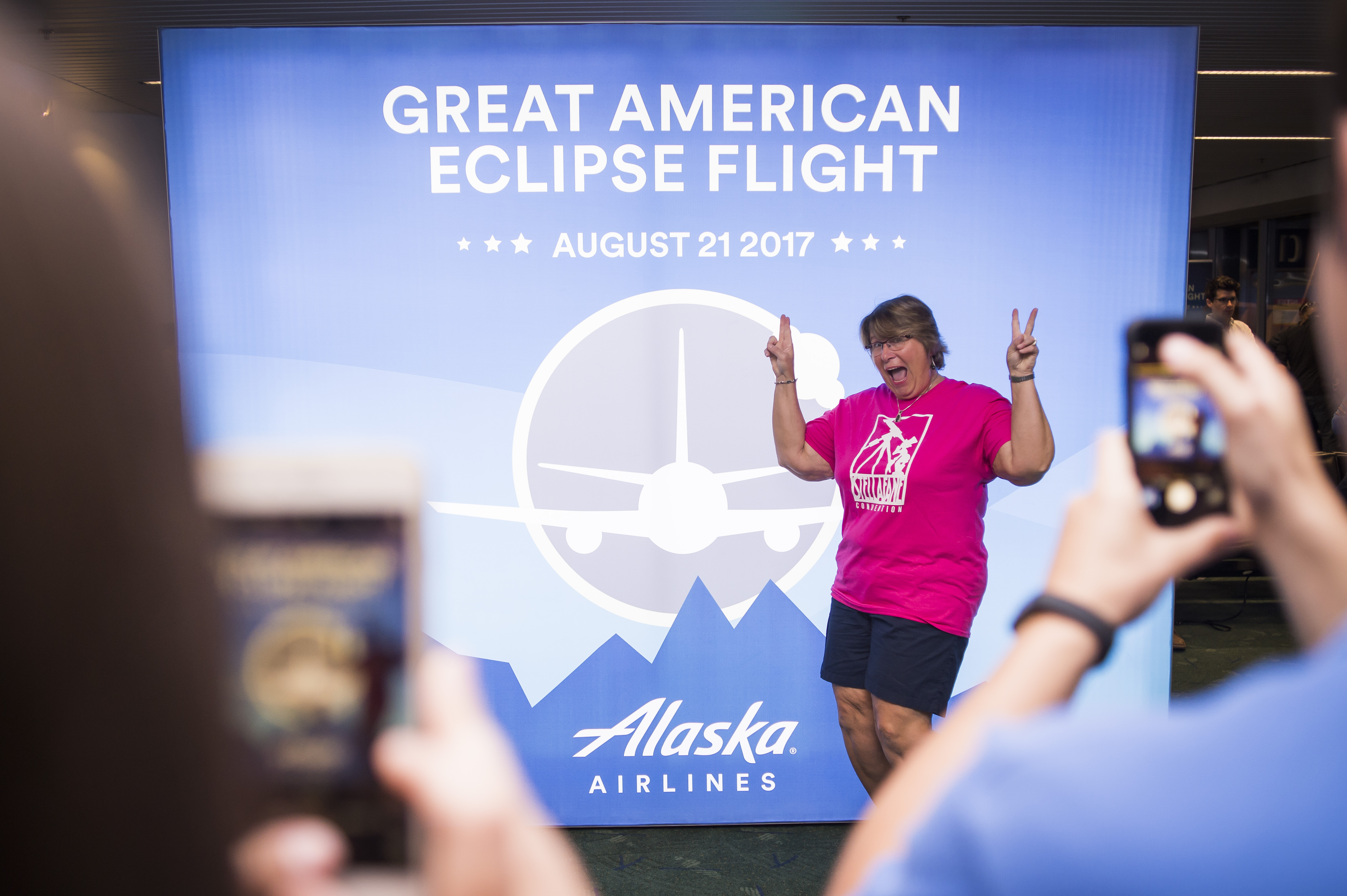 Kimberly Cassia stands in front of the Great American Eclipse Flight poster at the gate while onlookers snap photos.