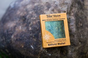 This is a photo of a packaged Tidal Vision Alaska Salmon Leather wallet sitting on a beach rock.