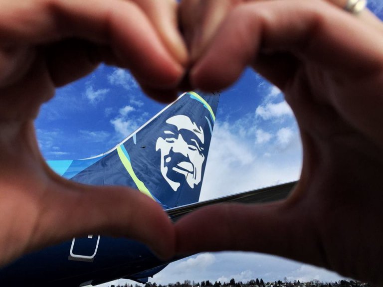 Photo of a person's hands forming a heart around the tail of an Alaska Airlines jet.