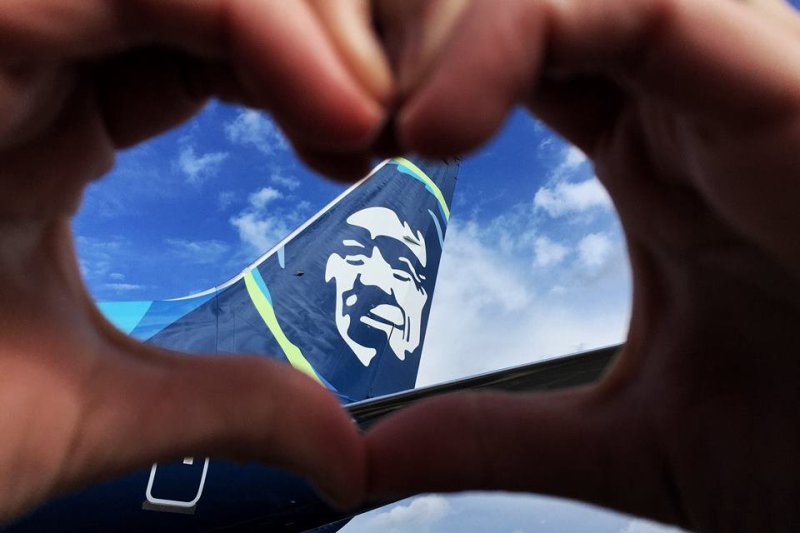 Photo of a person's hands forming a heart around the tail of an Alaska Airlines jet.