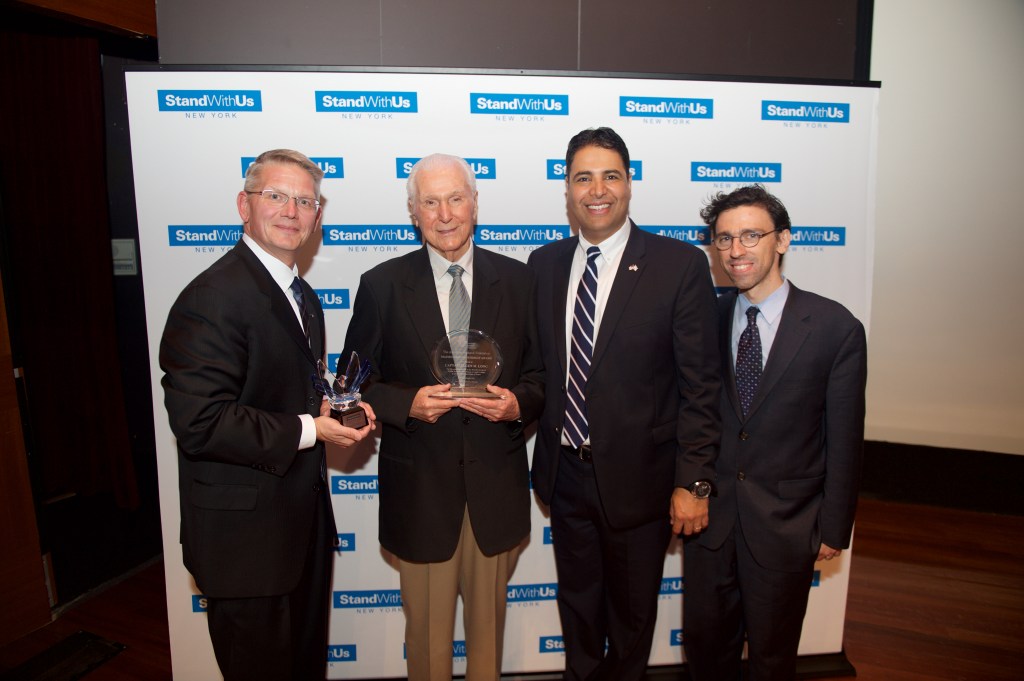 This is a photo of four men standing in front of a "StandWithUs" backdrop. The two men on the left are holding awards.