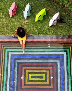 This is a photo of a woman dipping her feet into a small square pool that is painted in rainbow colors.