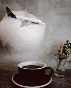 This is a photo of an Alaska Airlines mini plane embedded in cotton candy hanging over a cup of coffee.