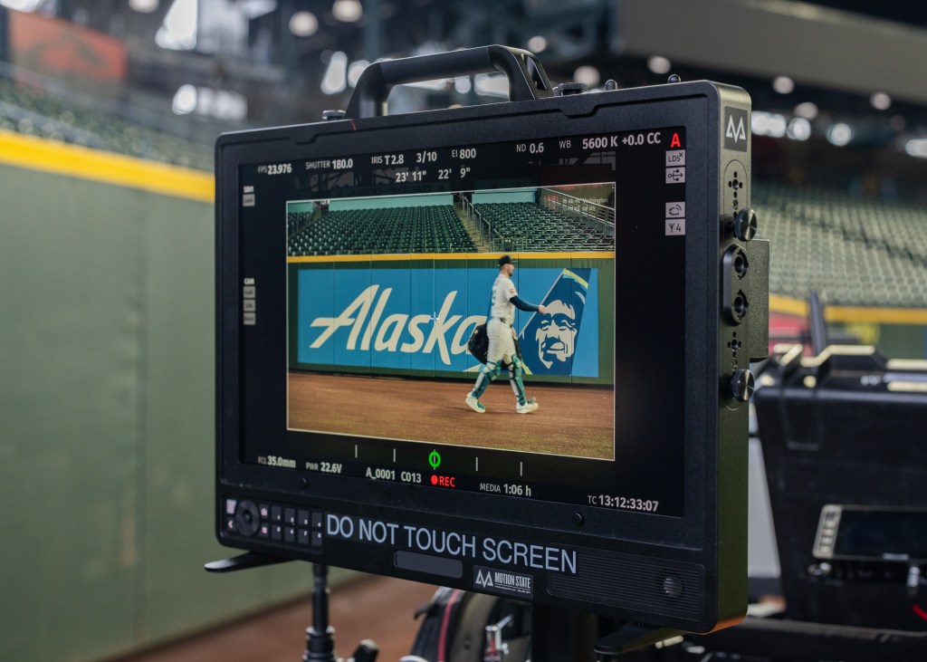 Photo looking Through the viewfinder of a camera at Cal Raleigh walking past an Alaska Airlines sign at T-Mobile Park